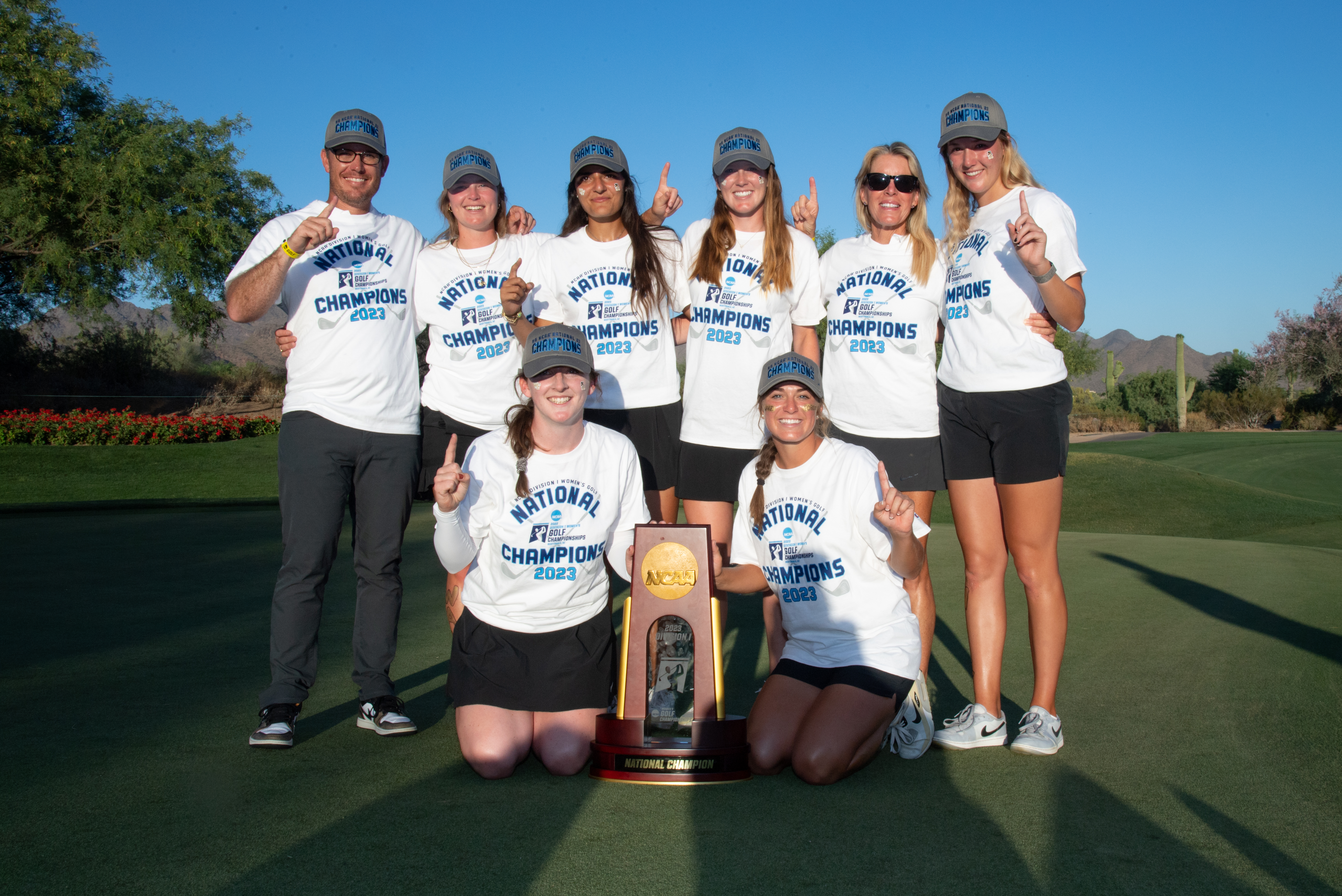 Photo of the women's golf team and coaches in their national championship shirts with their trophy